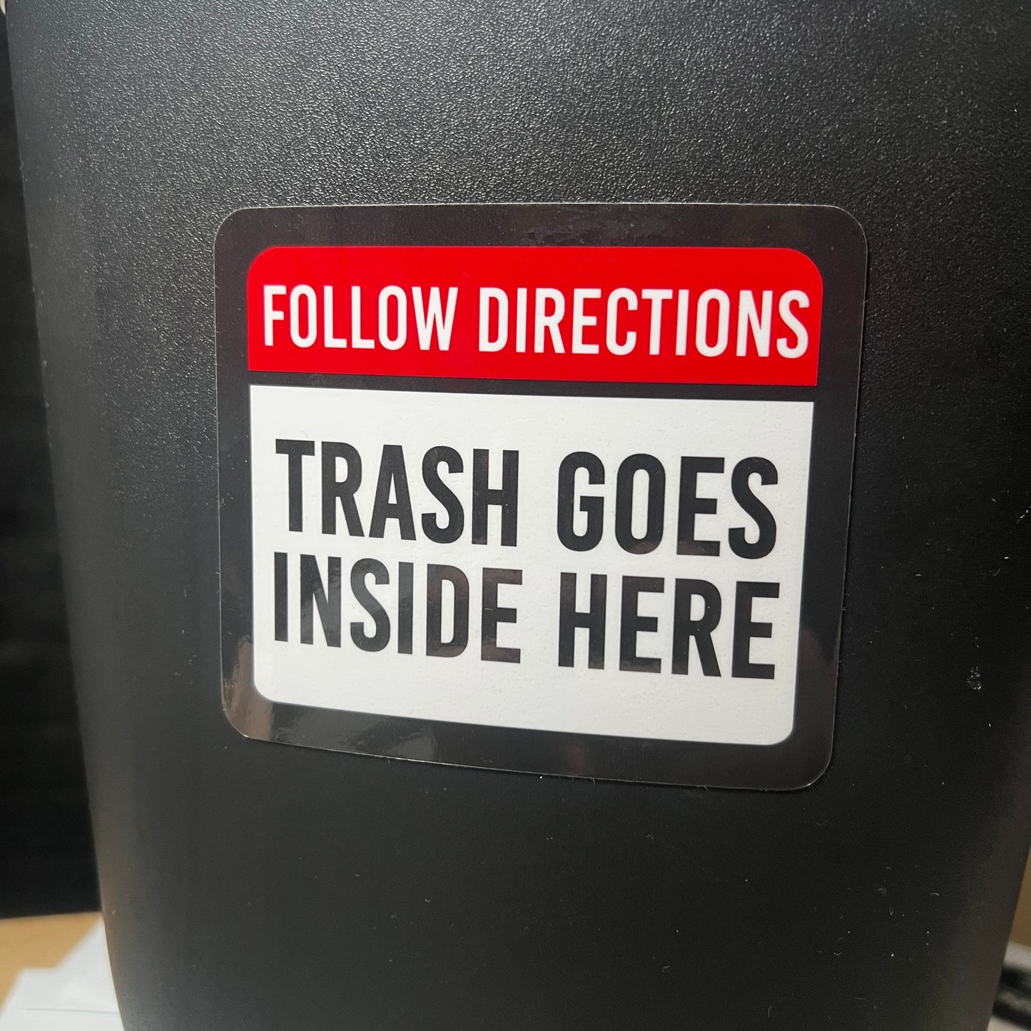 A picture showcasing a custom label on a trash can that says, " Follow Directions, Trash Goes Inside Here".