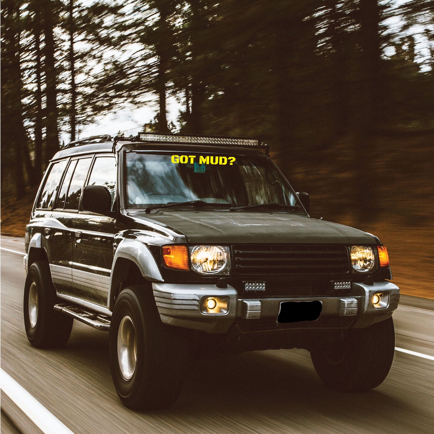 A car driving down a road with a custom text banner in yellow saying, "Got Mud?".