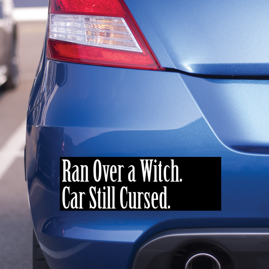 Blue car with a humorous text decal on the back. It says "Ran over a witch. Car still cursed.".
